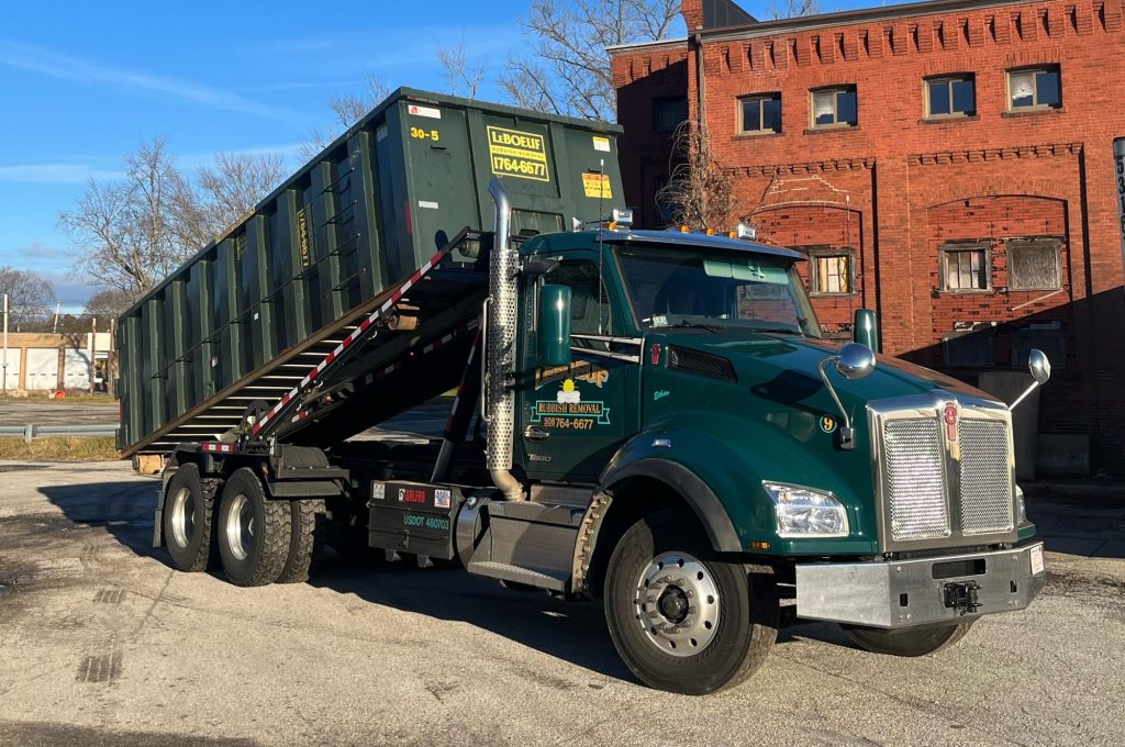 LeBoeuf roll-Off truck with a dumpster loading onto the back.