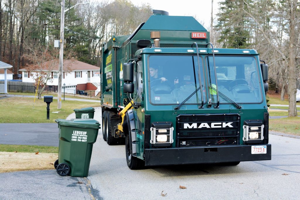 A LeBoeuf side-loading truck moves alongside a garbage bin for pickup.