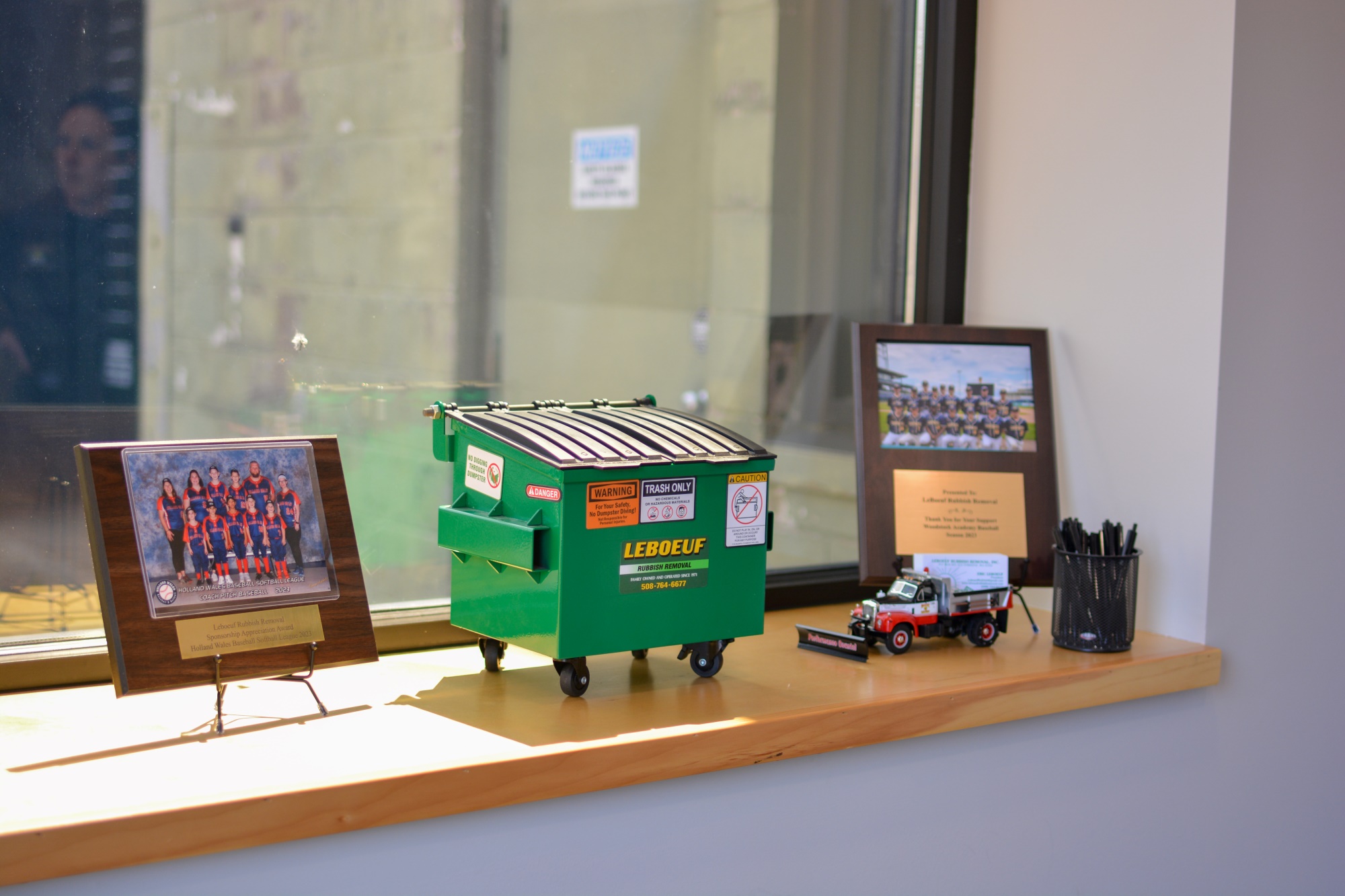 Closeup of a toy LeBoeuf commercial dumpster next to plaques of sports teams we support.