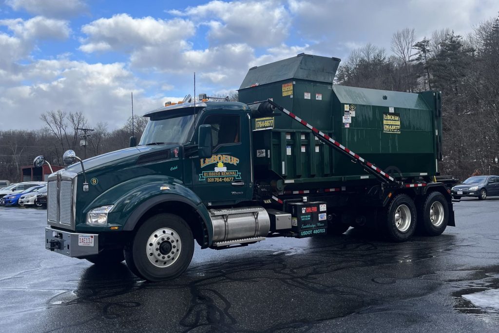 While smaller hook trucks handle 10and 15-cubic-yard containers, larger open-topped dumpsters and other units, like this compactor-with-container, require the use of longer-body roll-off trucks with a more robust frame and powerful hydraulic systems.]