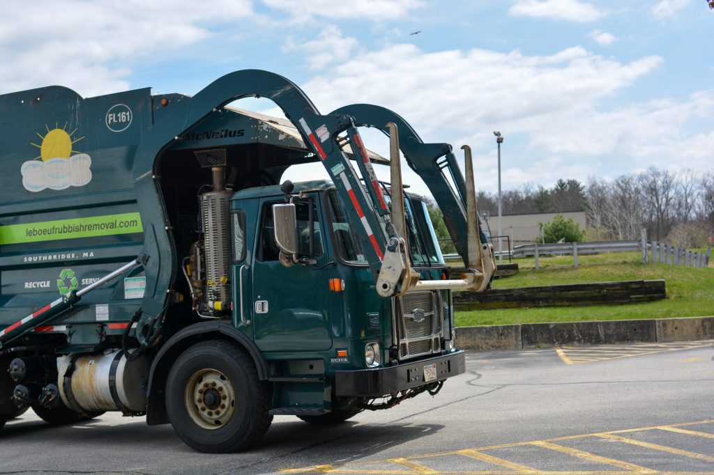 A LeBoeuf Rubbish Removal garbage truck preparing to pick up a dumpster on school grounds.