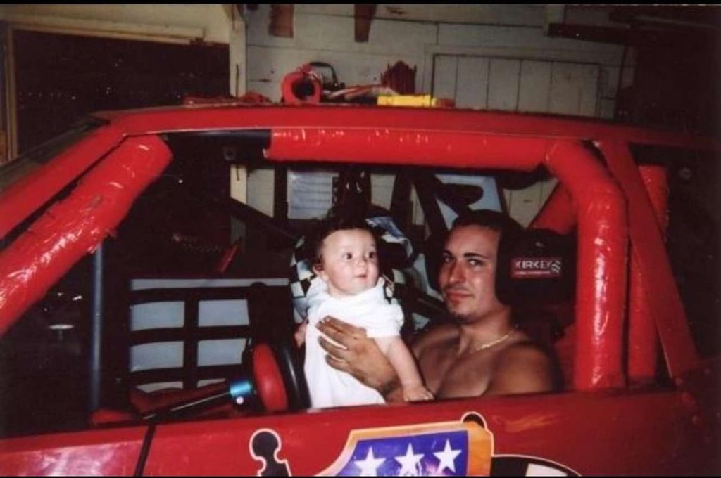 Trinity Provost as a baby being held by her father in his racing car.